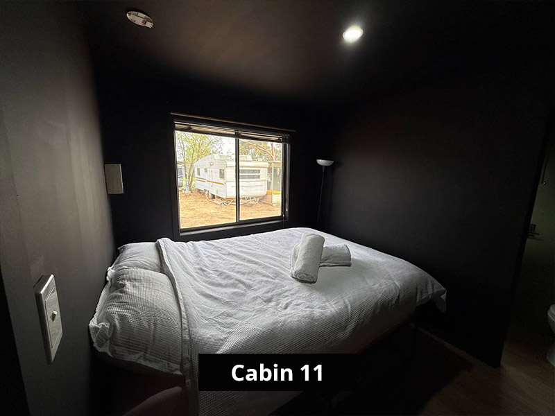 Queen bed in Cabin 11 with fresh linen and natural light, perfect for families or groups.